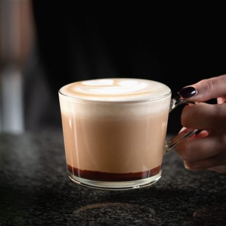 Female barista expertly combines espresso, rich chocolate, and creamy goodness, creating a delightful mocha topped with a pour of indulgent chocolate.
