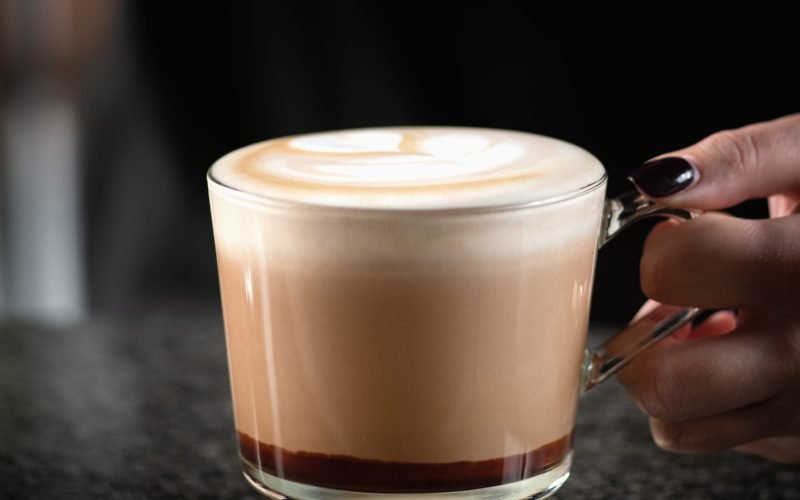Female barista expertly combines espresso, rich chocolate, and creamy goodness, creating a delightful mocha topped with a pour of indulgent chocolate.