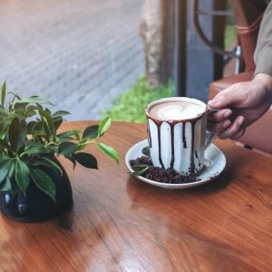 closeup-image-of-a-hand-holding-a-cup-of-hot-chocolate-on-wooden-table-in-cafe.jpg