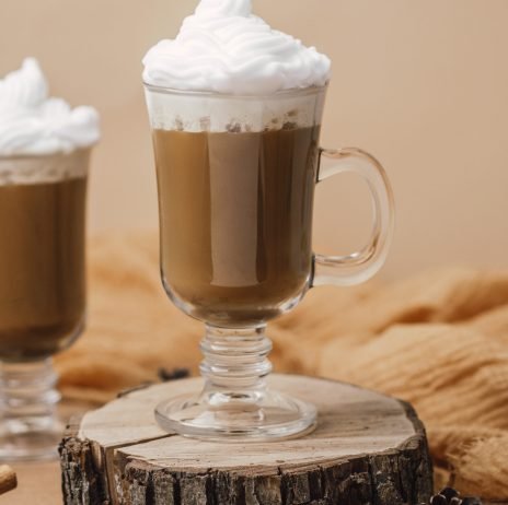 Hot chocolate drink with whipped cream in glass cup on wood slice cozy setting