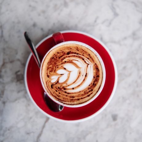 Latter art, rosetta flower on a foamy cappuccino, on a red cup at a cafe.